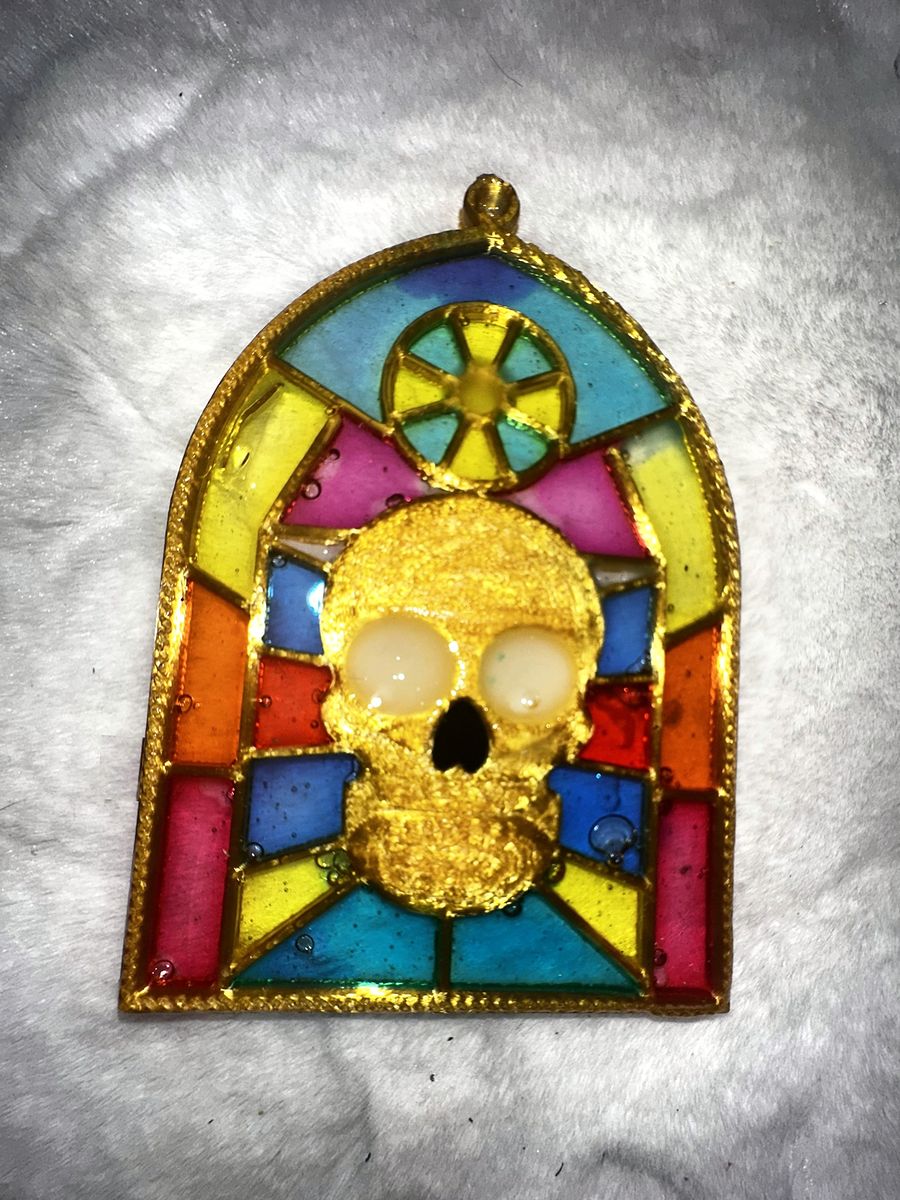 Gothic Skull Window ornament in daylight: a gold skull inside an arched stained-glass frame with red, yellow, blue and teal windows
